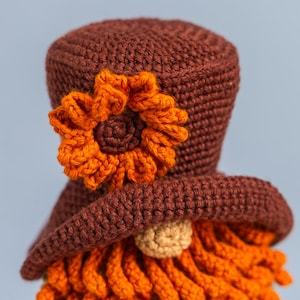 May include: A crocheted gnome with a brown hat, orange beard, and an orange flower on the hat.