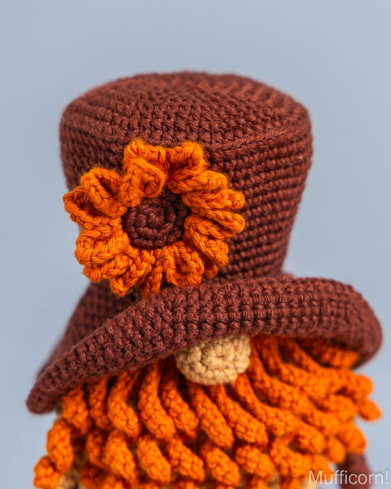 May include: A crocheted gnome with a brown hat, orange beard, and an orange flower on the hat.