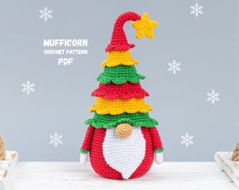 Può includere: Gnomo di Natale a forma di albero di Natale all'uncinetto con un cappello rosso, verde e giallo e una barba bianca. Il gnomo è in piedi su una superficie bianca. Il testo "MUFFICORN CROCHET PATTERN PDF" è visibile nell'immagine.