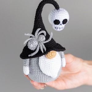 May include: A gray and white crocheted gnome with a black hat, a spider, and a white skull on top. The gnome has a white beard and a brown nose.