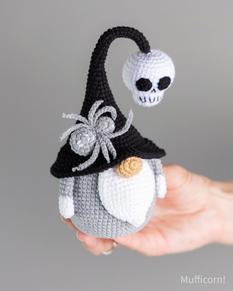 May include: A gray and white crocheted gnome with a black hat, a spider, and a white skull on top. The gnome has a white beard and a brown nose.