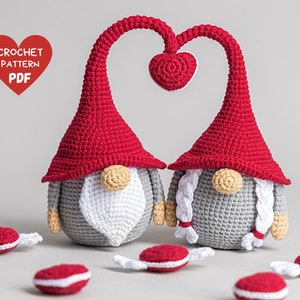 May include: Two crocheted gnomes in red and gray with white beards and braids. The gnomes are holding hands in the shape of a heart. The gnomes are surrounded by red and white candy canes.