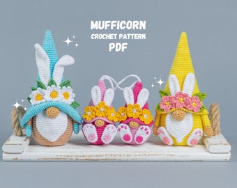 May include: Four crocheted gnomes with bunny ears and flower crowns. The gnomes are in blue, yellow, pink, and pink. The gnomes are sitting on a white wooden shelf. The text "MUFFICORN CROCHET PATTERN PDF" is above the gnomes.
