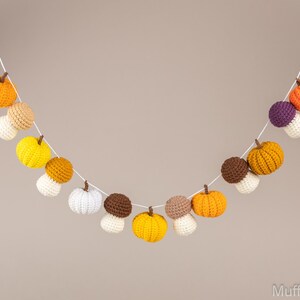 May include: A crocheted garland with alternating orange, yellow, and brown pumpkins and white mushrooms. The garland is strung on white twine.