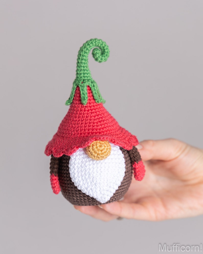 May include: A crocheted gnome with a red hat, brown body, white beard, and a green curly hat top.