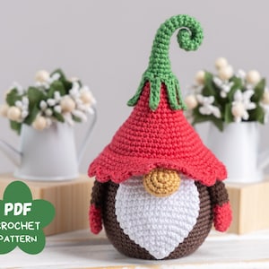 May include: Crochet pattern for a gnome with a red hat, white beard, and brown body. The gnome is wearing a green hat with a curled tip. The pattern is available as a PDF download.