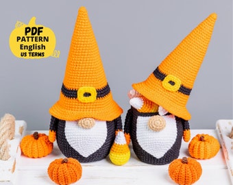 May include: Two crocheted Halloween gnomes with orange and black hats, white beards, and candy corn accents. The gnomes are sitting on a white surface with small orange pumpkins.