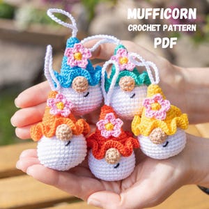 Puede incluir: Cinco adornos de gnomos de ganchillo coloridos con detalles de flores. Cada gnomo tiene un cuerpo blanco, un sombrero de diferente color y una pequeña flor en el sombrero. El texto "MUFFICORN CROCHET PATTERN PDF" es visible.