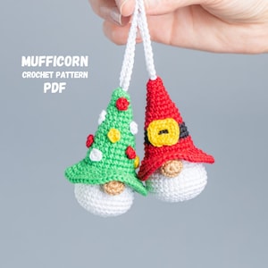 Könnte beinhalten: Zwei gehäkelte Gnom-Anhänger, einer mit einem grünen Weihnachtsbaumhut und der andere mit einer roten Weihnachtsmannmütze. Beide Gnome haben weiße Bärte und hängen an weißen Schnüren.