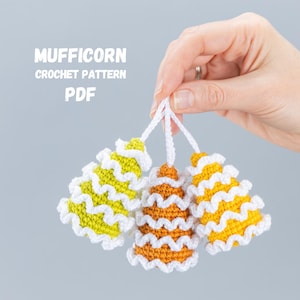 May include: Three crocheted Mufficorn ornaments in yellow, orange, and white. The ornaments are shaped like cones and have a wavy texture. The text "MUFFICORN CROCHET PATTERN PDF" is visible in the image.