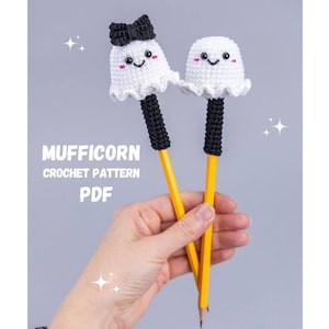 May include: Two yellow pencils topped with white crocheted ghost figures featuring black eyes, pink cheeks, and ruffled edges. One ghost wears a black crocheted bow. Text reads MUFFICORN CROCHET PATTERN PDF. The design is crafted with yarn.