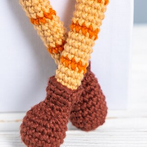 May include: Close-up of a crocheted toy with brown boots and orange and beige striped legs.