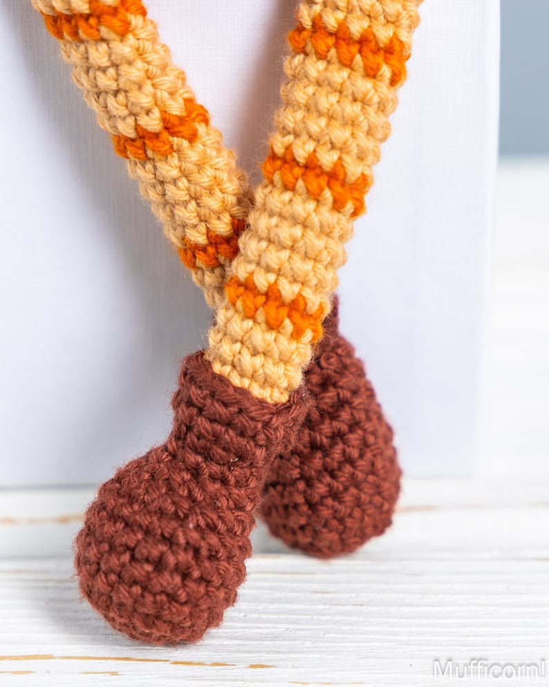 May include: Close-up of a crocheted toy with brown boots and orange and beige striped legs.