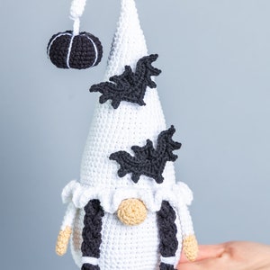 May include: White crocheted gnome with black yarn braids, a black crocheted pumpkin on top of its hat, and black crocheted bats on the hat.