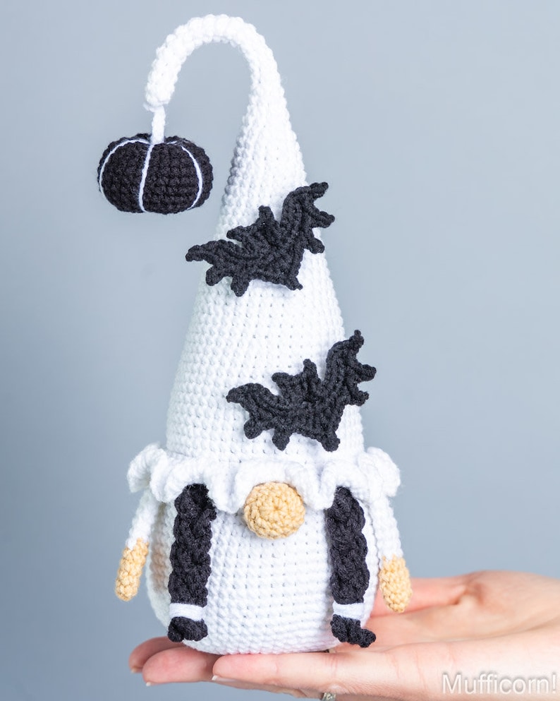 May include: White crocheted gnome with black yarn braids, a black crocheted pumpkin on top of its hat, and black crocheted bats on the hat.