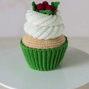 May include: A crocheted cupcake with green icing and a white swirl on top. The cupcake is decorated with red berries and green leaves.