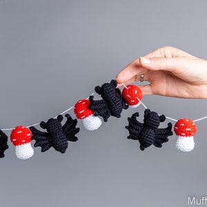 May include: A black and white crocheted bat and red and white crocheted mushroom garland. The garland is strung on a white string.