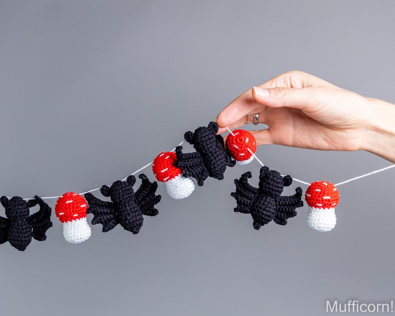 May include: A black and white crocheted bat and red and white crocheted mushroom garland. The garland is strung on a white string.