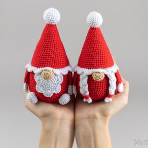 May include: Two crocheted gnomes with red hats and white beards. The gnomes are holding hands and have white pom-poms on their hats.