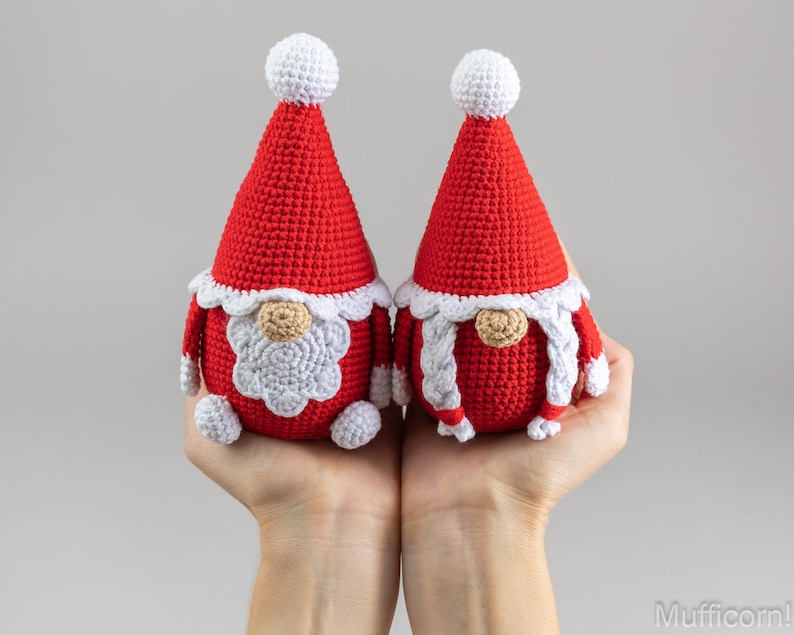 May include: Two crocheted gnomes with red hats and white beards. The gnomes are holding hands and have white pom-poms on their hats.