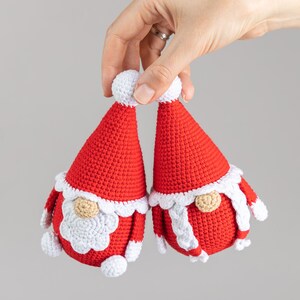 May include: Two crocheted gnome ornaments in red and white. The gnomes have white beards and white pom-poms on their hats.