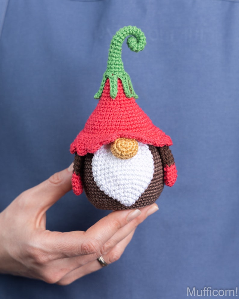 May include: A crocheted gnome with a red hat, brown body, white beard, and green curly hat top.