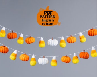 May include: A crochet garland with alternating orange pumpkins and yellow and orange candy corn. The garland is strung on a white string and hangs against a gray background. The text "PDF PATTERN English US TERMS" is written in black on an orange pumpkin shape.