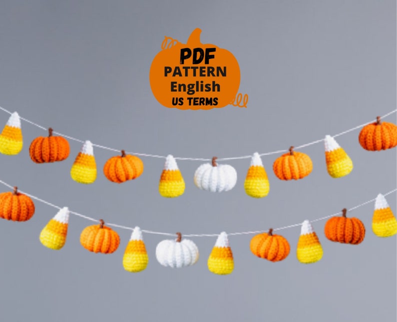May include: A crochet garland featuring alternating orange pumpkins and yellow and orange candy corn. The garland is strung on a white string and hangs against a grey background. The text "PDF PATTERN English US TERMS" is written in black on an orange pumpkin shape.