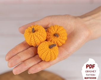 May include: Three crocheted orange pumpkins in a hand. The pumpkins have brown stems. The image includes the text "PDF CROCHET PATTERN MUFFICORN".