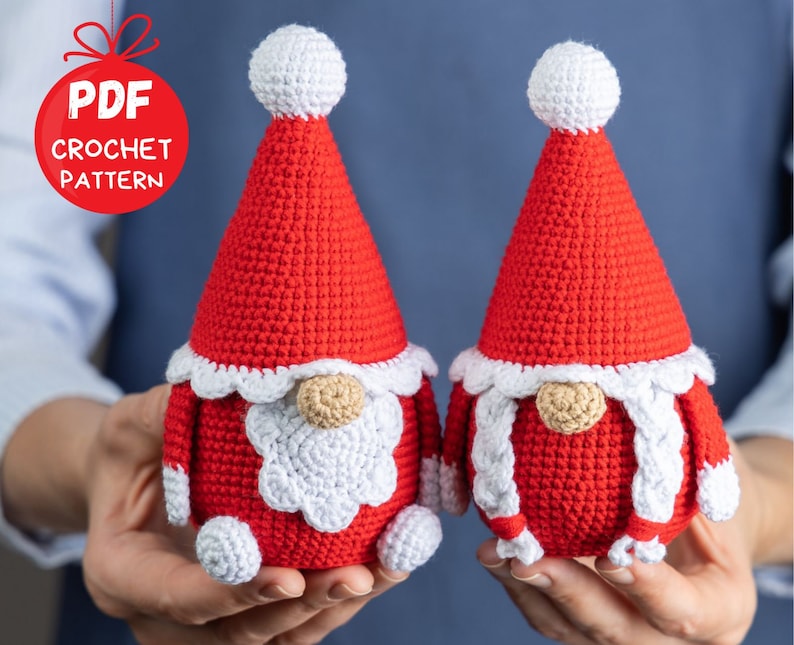 May include: Two crocheted gnomes wearing red hats with white trim. The gnomes have white beards and noses. The gnomes are being held by a person's hands. PDF CROCHET PATTERN is written on a red circle.
