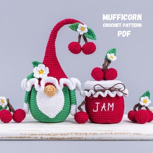 Puede incluir: Patrón de crochet para un gnomo rojo y verde con barba blanca y un tarro de mermelada rojo y blanco con la palabra "JAM" bordada. El gnomo sostiene una cereza y hay cerezas esparcidas alrededor del gnomo y el tarro.