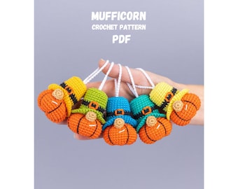 May include: A collection of handmade crochet ornaments in the shape of pumpkins with hats. The ornaments are orange, green, yellow, and blue, with white string hangers. The text "MUFFICORN CROCHET PATTERN PDF" is at the top.