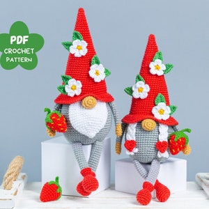 Op de afbeelding: Twee gehaakte gnomen met rode en witte hoeden versierd met bloemen. De gnomen houden aardbeien vast en zitten op een wit oppervlak. PDF Haakpatroon.