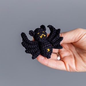 May include: A small black crocheted bat with yellow embroidered eyes and a star on its chest.