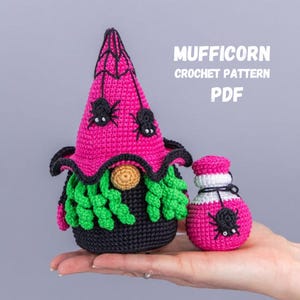 May include: A crocheted gnome and potion bottle in pink, black, green, and tan. The gnome has a pink hat with a spiderweb design and spiders. The potion bottle is pink with a spider. Text on the image reads "MUFFICORN CROCHET PATTERN PDF".