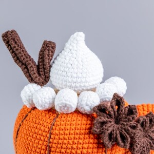 Puede incluir: Primer plano de una calabaza de ganchillo con la parte superior blanca y el tallo marr&oacute;n. La calabaza es naranja con l&iacute;neas verticales. Pompones blancos y una flor marr&oacute;n acent&uacute;an el dise&ntilde;o. La palabra "Mufficorn!" est&aacute; en la esquina inferior derecha.