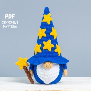 May include: Crochet pattern PDF for a blue and yellow gnome wearing a pointed hat with stars. The gnome is holding a brown and yellow wand.