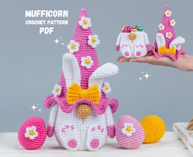 May include: A pink and white crocheted gnome with bunny ears and a yellow bow. The gnome is holding a basket filled with colorful Easter eggs. The gnome is sitting on a white surface with other crocheted Easter eggs.