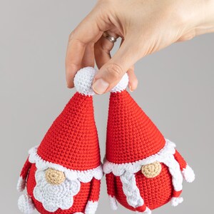 May include: Two crocheted gnome ornaments in red and white. The gnomes have white beards and white hats with red pom-poms.