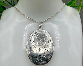 Puede incluir: Un collar con un medallón ovalado de plata con un intrincado diseño floral. El medallón cuelga de una delicada cadena y se exhibe en un maniquí blanco. Una pieza de joyería clásica.