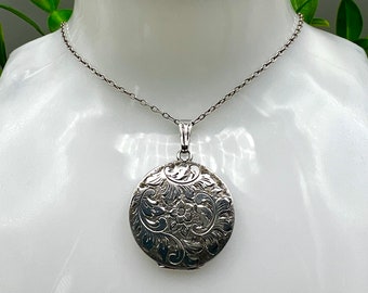 May include: A silver locket necklace with a round pendant featuring an intricate floral design.