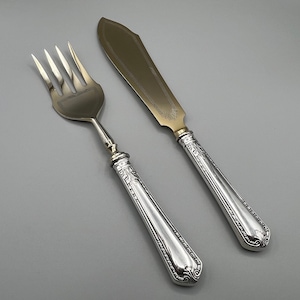 Puede incluir: Un juego de servicio de plata con un tenedor y un cuchillo. Los mangos son ornamentados y tienen un acabado plateado. La hoja del cuchillo es ligeramente curvada y tiene un acabado dorado.