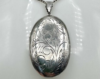 Puede incluir: Un collar de plata con un medallón de forma ovalada que presenta un intrincado diseño floral.