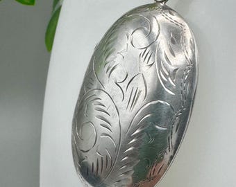 Puede incluir: Colgante ovalado de plata con intrincado grabado floral. El colgante cuelga de una delicada cadena de plata. El diseño grabado cubre toda la superficie del colgante, creando un aspecto detallado y elegante. Una pieza de joyería clásica.
