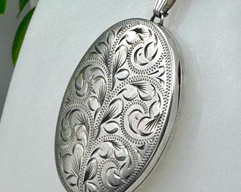 Puede incluir: Colgante de plata ovalado con grabado floral detallado. El medallón cuelga de una fina cadena de plata. El diseño presenta hojas y patrones arremolinados. El medallón se muestra sobre un fondo blanco.