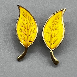 Puede incluir: Un par de pendientes de hoja amarilla con un contorno dorado y un patrón de vetas detallado.