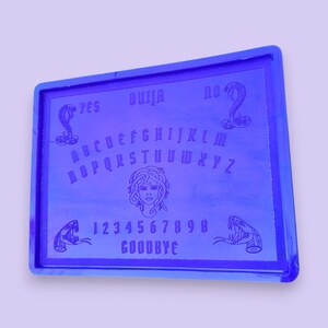 Peut inclure: Un plateau de Ouija en plastique bleu avec un motif de tête de Méduse et des accents de serpent. Le plateau comporte les lettres de l'alphabet, les chiffres de 1 à 9 et les mots "YES", "NO" et "GOODBYE".