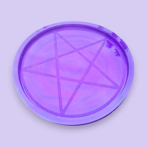 Pode incluir: Uma bandeja redonda de cor roxa com um design de estrela de cinco pontas. A bandeja é feita de resina e tem um acabamento brilhante.