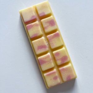 May include: A white wax melt bar with pink swirls and glitter. The bar is divided into 12 squares.