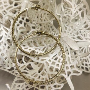 May include: A pair of gold hoop earrings with a textured snake design. The earrings are on a white background.